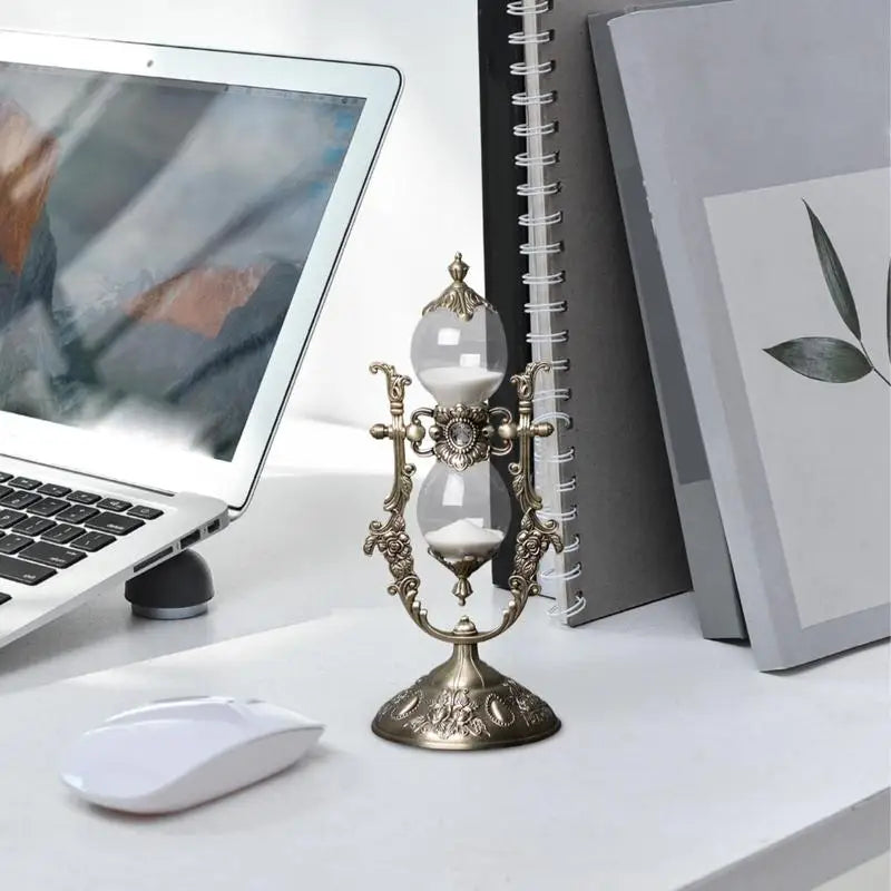 Hourglass sand timer on a desk beside a laptop